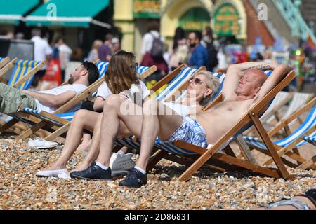 Ein kaukasisches Paar, das an einem heißen Frühlingstag in Brighton, East Sussex, England, in Liegestühlen am Strand sitzt. Stockfoto