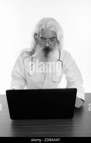 Studio shot der älteren bärtigen Mann Arzt mittels Laptop auf hölzernen Tisch Stockfoto