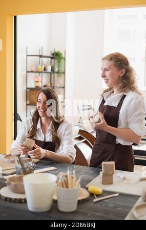 In der Tonwerkstatt. Töpferinnen sprechen und lächeln während des Arbeitsprozesses in der Tonwerkstatt. Weibliche Töpfer Meister Rollen den Ton auf Stockfoto