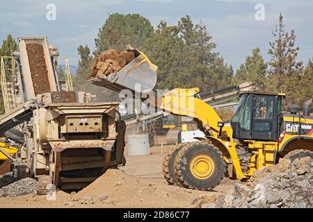 Ein großer, erdbeweglicher Traktor auf einer Baustelle in Bend, Oregon, bewegt Felsbrocken in einen Felsbrecher, um Kies zu machen. Die Baustelle ist für Stockfoto