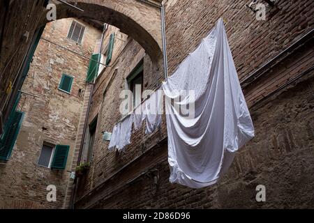 ITALIEN, TOSKANA, PROVINZ SIENA, SIENA - 07. Mai 2018: Straße von Siena, Backsteingebäude, Fenster mit grünen Fensterläden, Waschmaschine hängen an Fäden Stockfoto