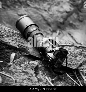 Schwarzes Super-Tele-Objektiv und Digitalkamera-Gehäuse flach lag auf alten log. Draufsicht. Selektiver Fokus. Stockfoto