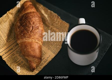 Blick auf frisch gebackene Croissants auf einem Stück Zeitung Mit einer Tasse heißen Kaffee einfache Frühstück Kopie Leerraumnachricht Stockfoto