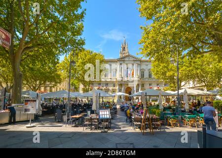 Outdoor-Cafés mit Touristen sitzen unter Sonnenschirmen vor dem Rathaus in der Stadt Avignon, Frankreich, in der Provence Region. Stockfoto