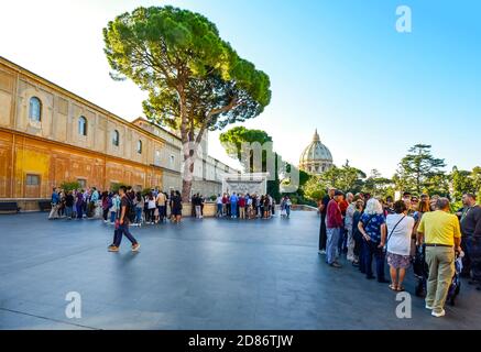 Die Reisegruppen versammeln sich in separaten Bereichen auf dem Dach des Vatikanischen Museums mit der Kuppel des Petersdoms in der Ferne. Stockfoto