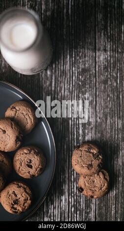 Flaches Lay of Chocolate Chip Cookie und eine Flasche Milch mit Krümel auf Holztisch einfaches Frühstück Snack c Stockfoto