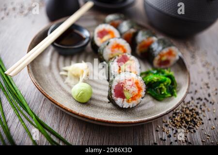 Sushi-Maki-Rollen mit Thunfisch, fliegender Fischkaviar, Krabben, Avocado auf einem Teller mit Essstäbchen, Sojasauce, Wasabi und Ingwer. Traditionelles japanisches Essen Stockfoto