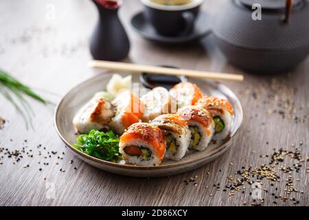 Sushi-Maki-Brötchen mit Lachs, Aal, Avocado, Gurke auf einem Teller mit Essstäbchen, Sojasauce, Wasabi und Ingwer. Japanische traditionelle Fischgerichte aus der Nähe Stockfoto