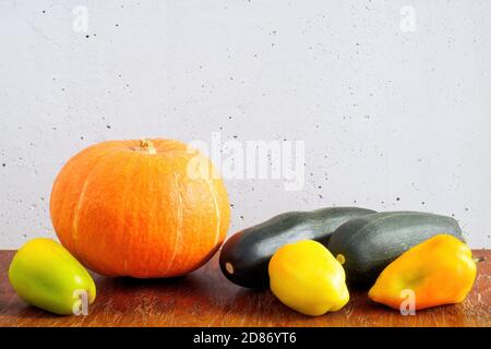 Orangefarbener Kürbis, dunkelgrüne Zucchini und Paprika auf Holztisch auf grauem Betonwandhintergrund. Speicherplatz kopieren Stockfoto