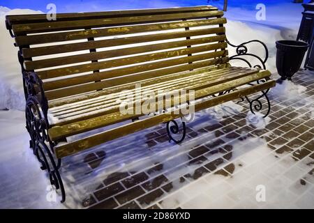 Leere braune Holzbank unter Lampenlicht am Winterabend Im Stadtpark Stockfoto