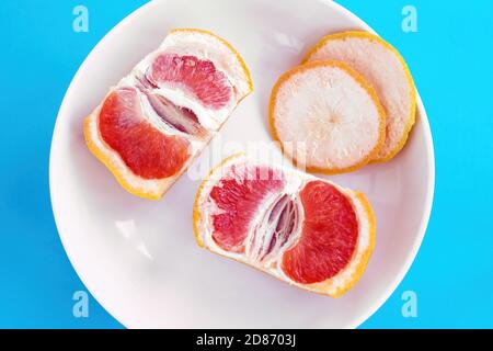 Zwei Hälften der geschnittenen Grapefruit auf weißem Teller auf blauem Hintergrund. Diät-Konzept, Draufsicht Stockfoto