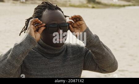 Junger schöner afrikanischer Mann mit geflochtener Sonnenbrille am Sandstrand im Winter. Hochwertige Fotos Stockfoto