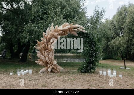 Hochzeitsbogen im Park mit vielen Kerzen daneben. Hochzeitsbogen. Ort der Hochzeitszeremonie Stockfoto