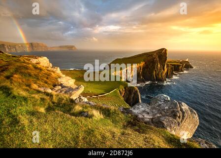 Ikonischer Leuchtturm der Isle of Skye am Neist Point mit wunderschönem goldenen Licht und Regenbogen über der Küste. Stockfoto