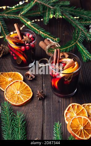 Weihnachtlicher Glühwein mit Preiselbeeren, Orange und Gewürzen auf rustikalem Holzhintergrund. Traditionelles warmes Getränk im Winter. Stockfoto