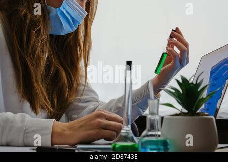 Die Wissenschaftlerin schaut auf eine Laborröhre. Kolben mit grüner und blauer Flüssigkeit in der Nähe der Pflanze. Forschung Virus Heilung Stockfoto