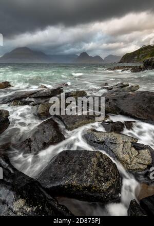 Dramatische Cuillin-Seewandschaft mit dunklen Sturmwolken und krachenden Wellen auf Felsen im Vordergrund. Elgol, Isle of Skye, Schottland, Großbritannien. Stockfoto