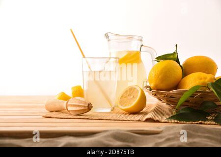 Frühstück mit Krug und Glas gefüllt mit frisch gepresstem Zitronensaft mit Obst auf Holzsockel am Strand. Vorderansicht. Horizontale Zusammensetzung. Stockfoto