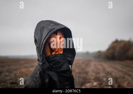 Eine Kürbis-Kopf Figur Halloween Jack-o'-Laterne mit einem gruseligen Gesicht in Eine schwarze Kapuzenrobe steht auf dem Feld Stockfoto