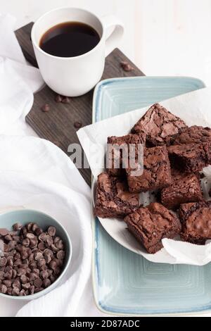 Kauende Schokoladensplitter-Brownies auf blauem Teller mit frischer Tasse Kaffee Stockfoto