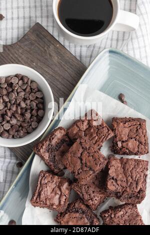 Kauende Schokoladensplitter-Brownies auf blauem Teller mit frischer Tasse Kaffee Stockfoto