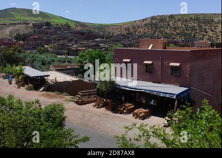 Rot verputztes Haus mit einem überdachten Außenstand mit Steinguttöpfen und Kannen in einer Straße im Ourika-Tal in der Nähe von Marrakesch, Marokko Stockfoto