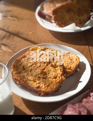 Vertikales Bild eines französischen Toasts in Nahaufnahme mit Milch und Wurstscheiben auf einem Holztisch. Stockfoto