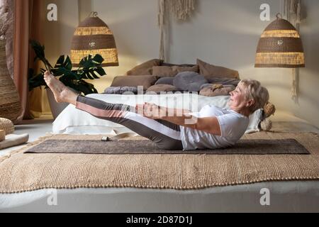 Sportliche ältere kaukasische Frau macht Übungen für abs, Ardha navasana, halbe Boot Pose Stockfoto