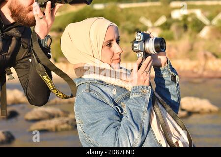 muslimischer Fotograf in Hijab, hält die Kamera und schaut hinein. Stockfoto