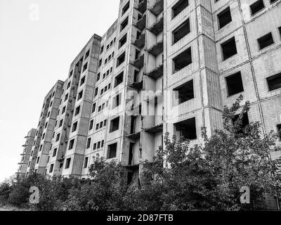 Hohe mehrstöckige verlassene sowjetische Gebäudefassade mit abgestürzten Balkonen in Schwarz und Weiß. Verwitterte Wohnsiedlung, unvollendete Stadt des nuklearen sie Stockfoto