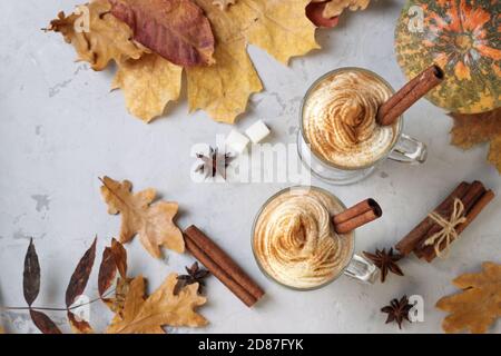 Zwei Glas-Tassen Kürbis Latte mit Gewürzen auf grauem Hintergrund mit Kürbissen und Herbstblättern. Draufsicht. Stockfoto