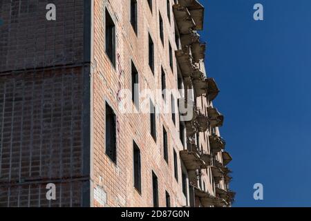 Hohe mehrstöckige verlassene sowjetische Gebäudefassade mit abgestürzten Balkonen. Verwittertes Haus am sonnigen Tag, unvollendete Stadt der Atomwissenschaftler in Birky Stockfoto