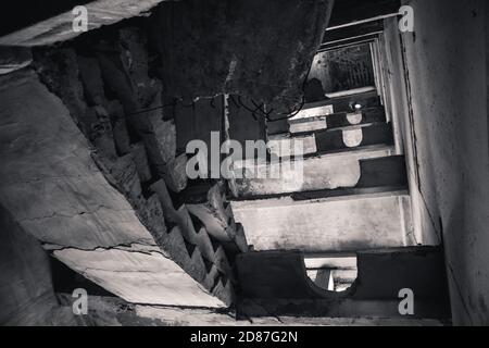 Schwarz und weiß zerschmetterte Betontreppe im verlassenen zerstörten Gebäude. Blick auf das zerstörte verwitterte mehrstöckige Haus Stockfoto