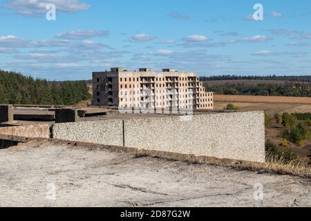 Blick vom Betondach des hohen mehrstöckigen verlassenen sowjetischen Gebäudes mit Blick auf ein anderes Haus mit hellblauer Landschaft. Unvollendete Stadt von nuclea Stockfoto