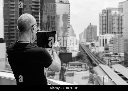 Rückansicht des kahlen Senior touristische Mann mit digitalen Tablet die Ansicht der Stadt in Bangkok, Thailand Stockfoto