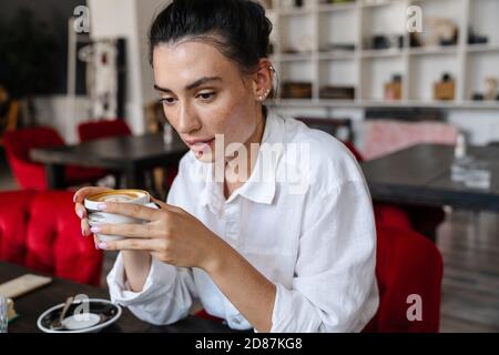 Selbstbewusste junge Geschäftsfrau hält eine Tasse Kaffee, während sie im Sitzen sitzt Café Stockfoto