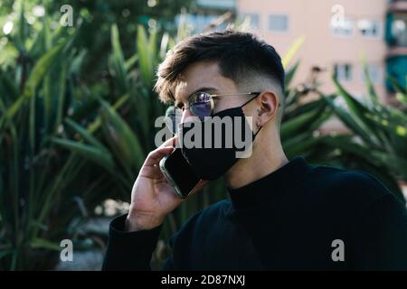 Junge mit Sonnenbrille und Maske Anrufe am Telefon Stockfoto