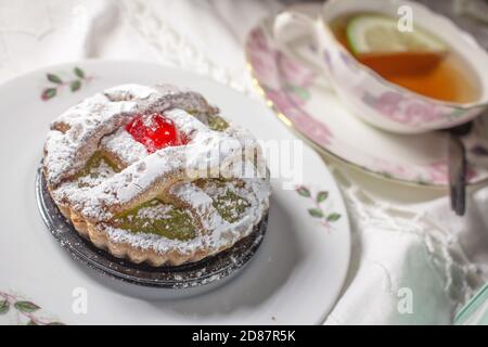 Eine besondere Süßigkeit aus Palermo namens 'Maria Stuarda', eine kleine Tarte mit sizilianischer Kürbismarmelade und kandierter Kirsche und einer Tasse Tee Stockfoto