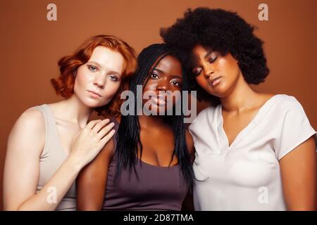 Junge hübsche kaukasische, afro, skandinavische Frau posiert fröhlich zusammen auf braunem Hintergrund, Lifestyle diverse Nationalität Menschen Konzept Stockfoto