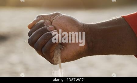 Nahaufnahme, schwarzer Mann Hand gießt Sand. Low-Angle-Aufnahme. Hochwertige Fotos Stockfoto