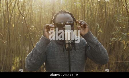 Junger affrikanischer Mann singt in der Natur, Sonnenstrahlen kommen durch die Bäume. Hochwertige Fotos Stockfoto