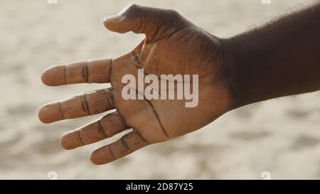 Sand in den Händen der Männer. Nahaufnahme von Sand, der durch die Hände eines Mannes läuft. Sand fällt von der Hand. Hochwertige Fotos Stockfoto