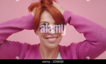 Porträt einer schönen Frau mittleren Alters mit herzförmigen Brille hält ihre roten Haare mit Händen. Beauty Shot. Hochwertige Fotos Stockfoto