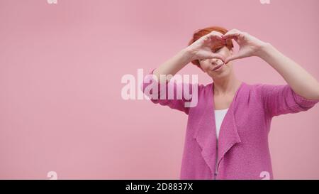 Rotschopf Frau in ihren 40er Jahren macht Herzform mit Händen. Isoliert auf violettem Hintergrund. Hochwertige Fotos Stockfoto