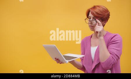 Verwirrt Rotschopf mittleren Alters Frau mit Laptop und Kreditkarte. Online-Shopping-Konzept. Isoliert auf orangefarbenem Hintergrund. Hochwertige Fotos Stockfoto