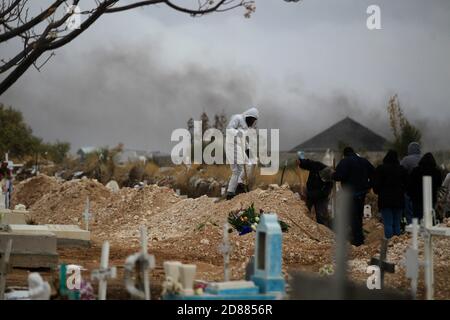 Ciudad Juarez, MEXIKO. Oktober 2020. Friedhofsarbeiter begraben die Leichen von Menschen, die mit COVID-19 infiziert wurden, in Ciudad Juarez, als eine Rauchsäule aus dem Krematorium des städtischen Friedhofs San Rafael aufsteigt. COVID-19 Opfer werden in einem separaten Teil des Friedhofs begraben. Heute erreichte Mexiko insgesamt 900,000 Fälle und fast 90,000 Todesfälle durch COVID-19. Quelle: Corrie Boudreaux/Alamy Live News Stockfoto