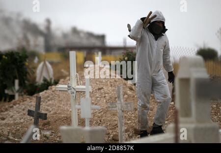 Ciudad Juarez, MEXIKO. Oktober 2020. Friedhofsarbeiter begraben die Leichen von Menschen, die mit COVID-19 infiziert wurden, in Ciudad Juarez, als eine Rauchsäule aus dem Krematorium des städtischen Friedhofs San Rafael aufsteigt. COVID-19 Opfer werden in einem separaten Teil des Friedhofs begraben. Heute erreichte Mexiko insgesamt 900,000 Fälle und fast 90,000 Todesfälle durch COVID-19. Quelle: Corrie Boudreaux/Alamy Live News Stockfoto