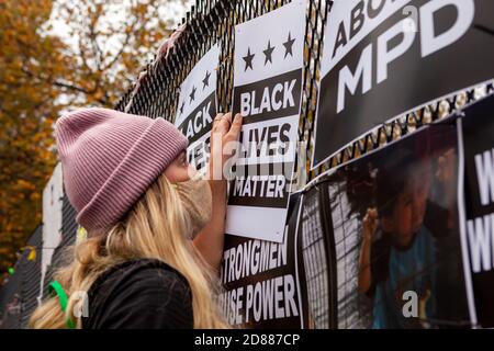 Washington, DC, USA, 27. Oktober 2020. Im Bild: Eine Frau hängt ein Black Lives Matter-Zeichen auf dem Lafayette Square Zaun während einer Veranstaltung, um den Zaun mit Protestkunst zu renovieren. Trump Anhänger zerstörten die existent Kunst in der Nacht des 26. Oktober 2020, als DC Polizisten zuschauten. Der Zaun ist mit Protestkunst bedeckt, seit er während der Proteste nach George Floyds Tod hochging. Kredit: Allison Bailey/Alamy Live Nachrichten Stockfoto