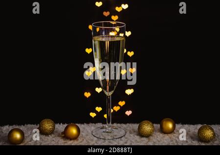 Ein Glas Sekt mit goldenen weihnachtsornamenten mit Liebe Form Bokeh Lichter auf dunklem Hintergrund. Stockfoto