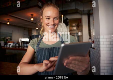 Glückliche weibliche Kellnerin im Café trägt Schürze mit digitalen Tablet Um Online-Bestellungen zu überprüfen Stockfoto